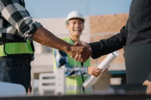 two men shaking hands at construction site with a smiling foreman in the background