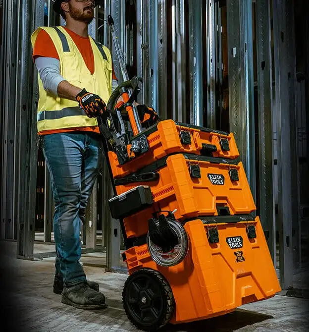 lifestyle shot of worker rolling big orange klein tools modbox mobile workstation