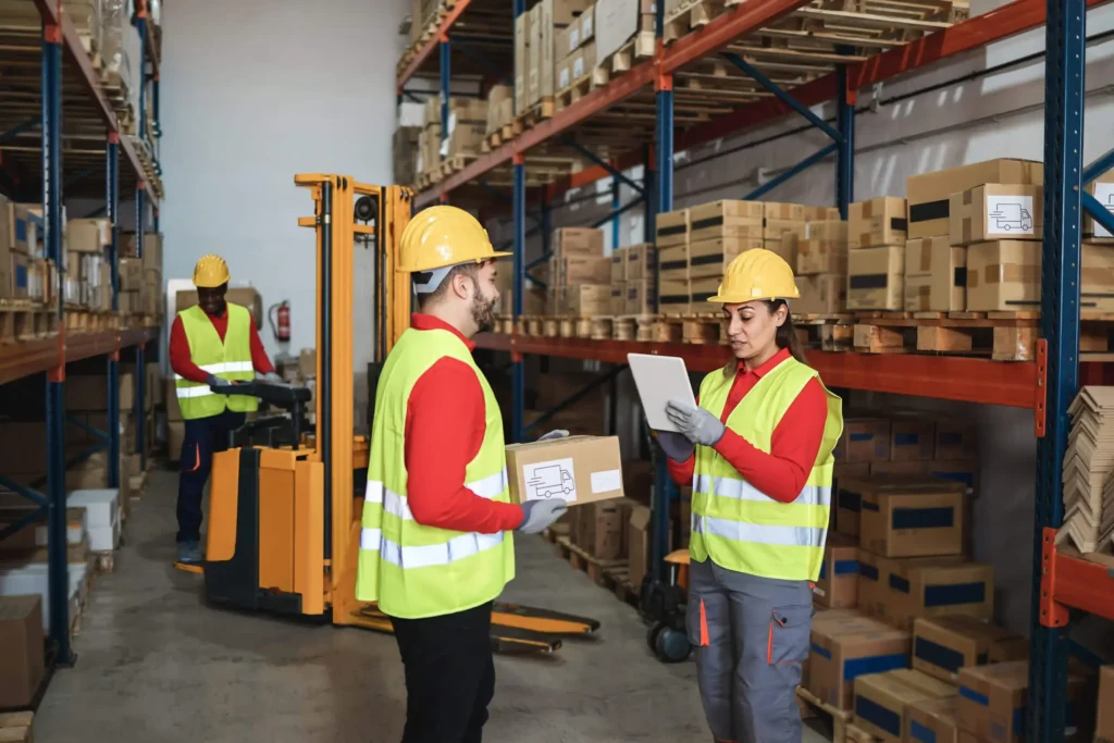 three employees in a warehouse. one is driving a forklift and two are checking products on a clipboard